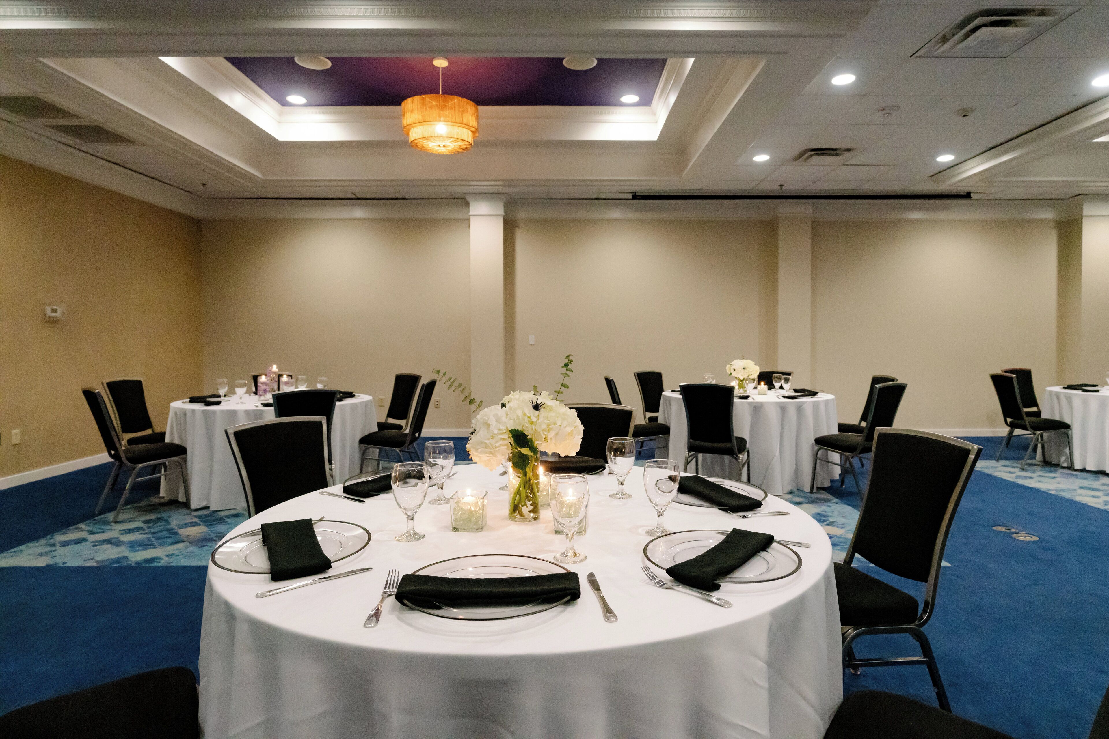 A conference room with round tables, black chairs, white tablecloths, and a chandelier.