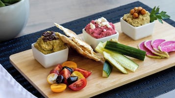 A wooden board with various food items including hummus, a flatbread, and sliced vegetables.