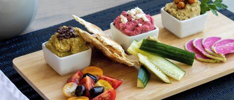 A wooden board with various food items including hummus, a flatbread, and sliced vegetables.