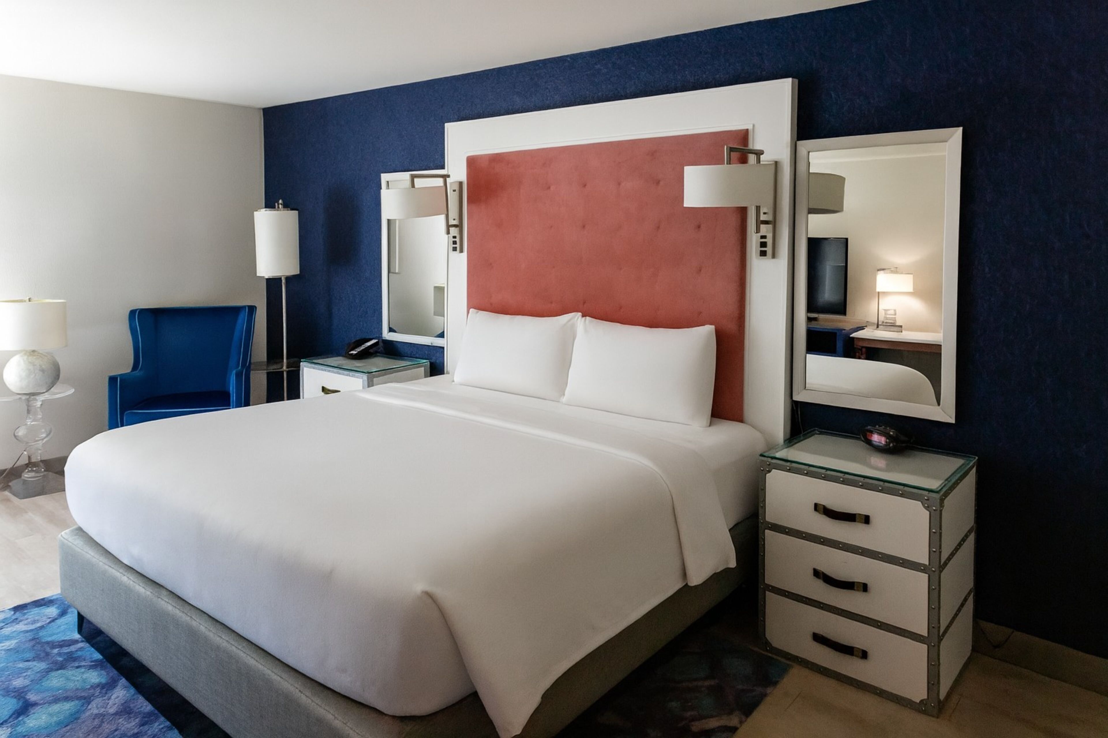 A hotel room with a large bed, a nightstand with a lamp, a chair, and a dresser.