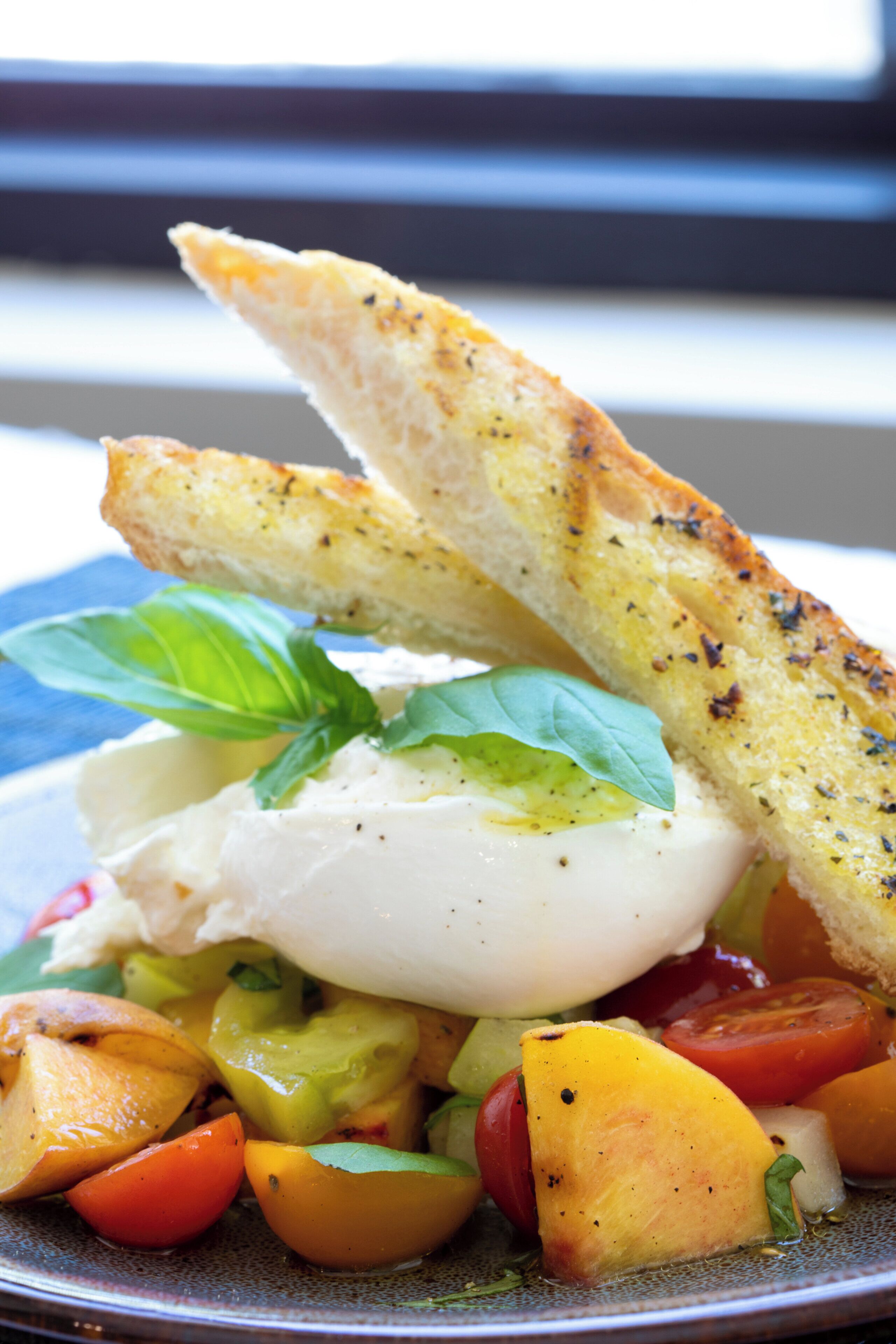 A plate of food with a poached egg, tomatoes, and basil on a ceramic plate.