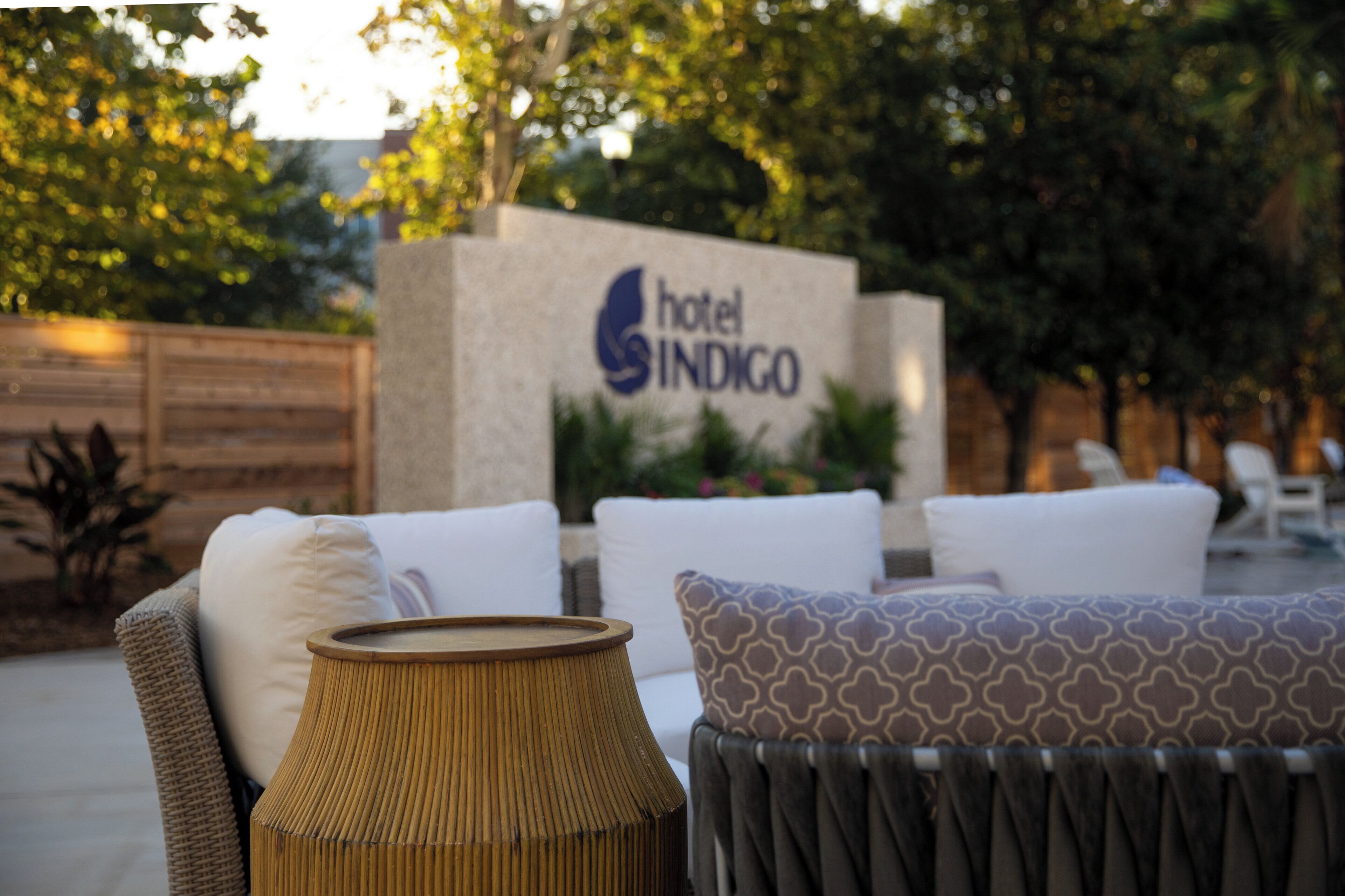 A hotel sign with the name 'Hotel Indigo' and outdoor seating with cushions and a woven table.