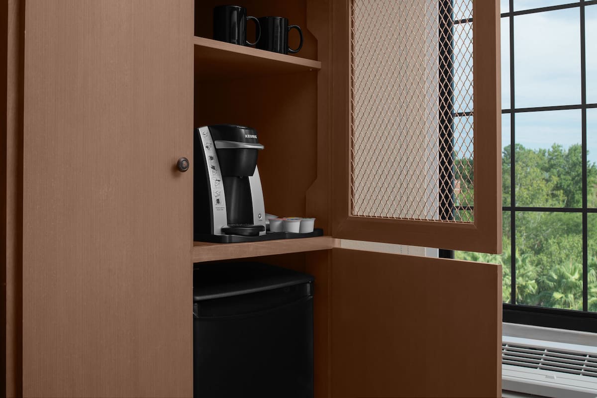 A kitchenette with a coffee maker, a trash bin, and a window with a view of greenery.