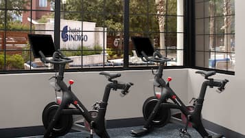 Two stationary bikes in a room with large windows overlooking a hotel sign.