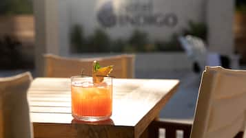 A wooden table with a glass of orange drink garnished with a mint leaf, set against a blurred background with a sign reading "Hotel Spinico".