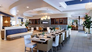 A modern restaurant with a long counter, multiple dining tables, and a seating area with sofas.