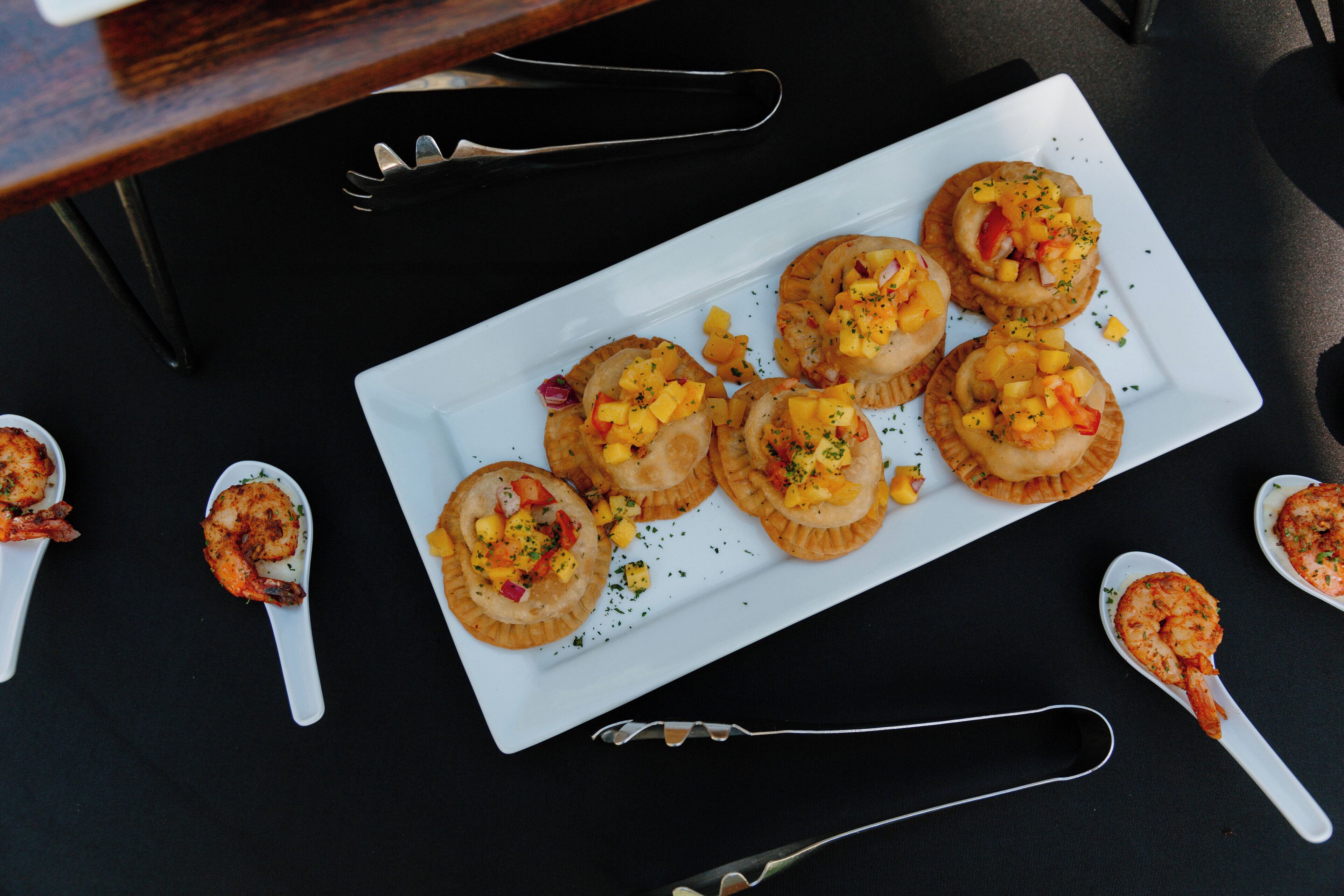 A white rectangular plate with six shrimp appetizers on a black table.