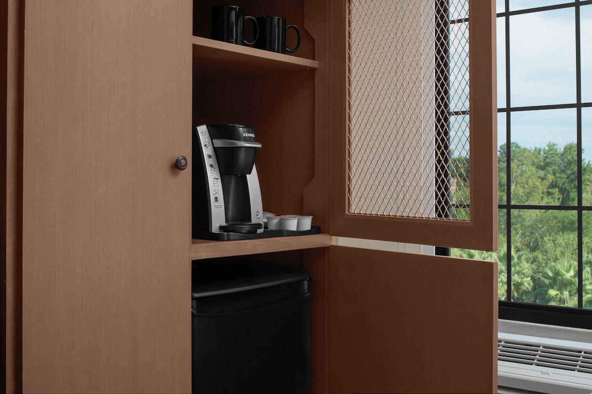 A coffee maker on a shelf, a trash bin, and a window with a view of trees.