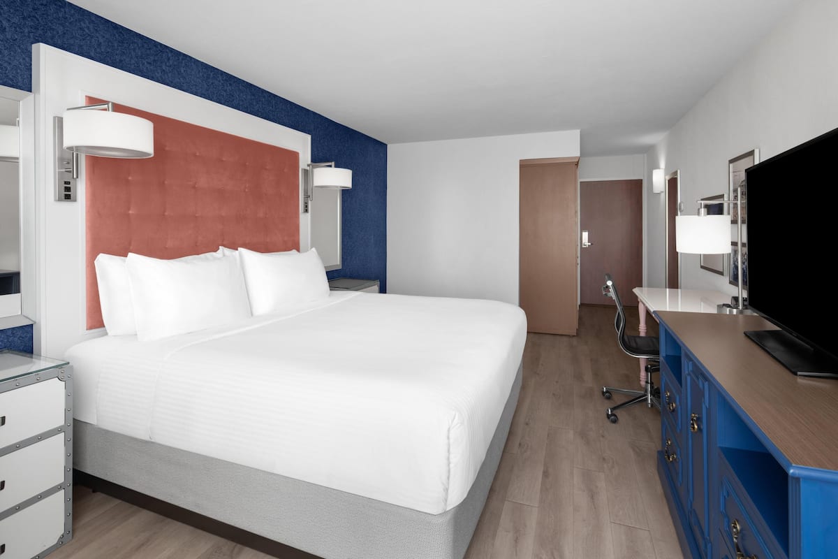 A hotel room with a large bed, a desk with a television, and a chair.