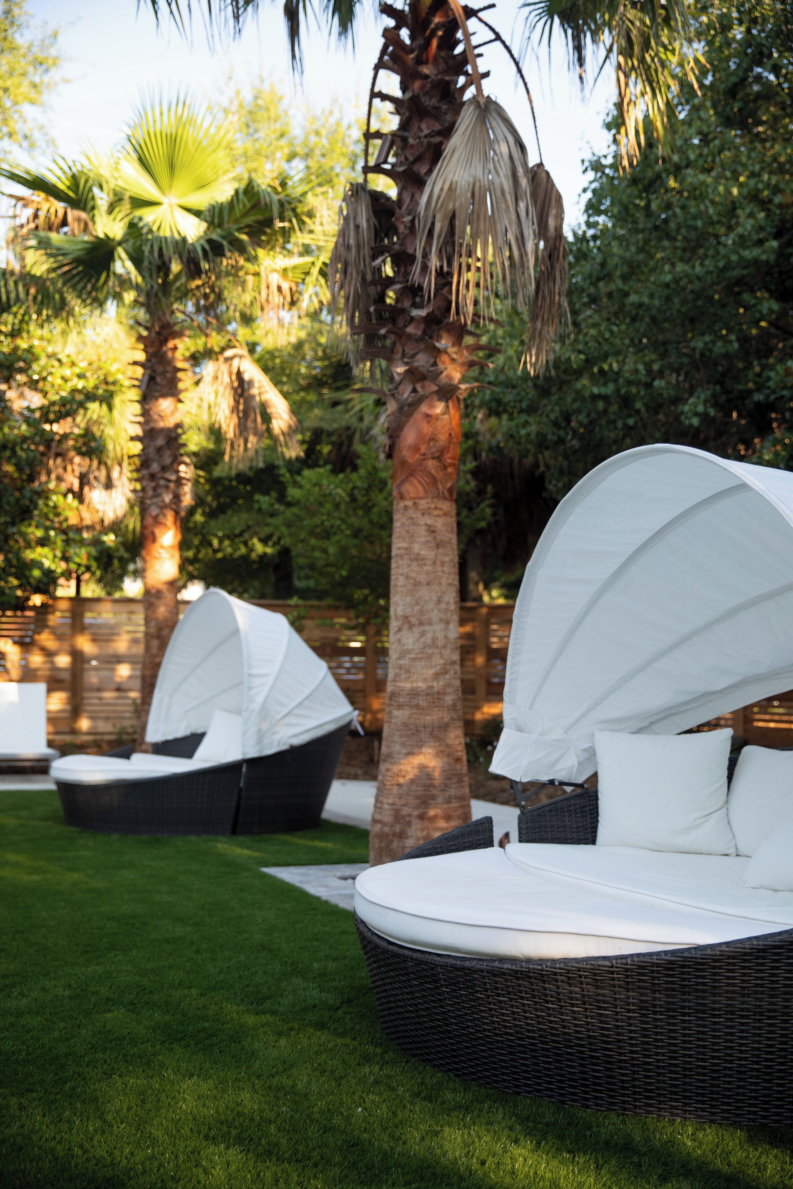A garden with outdoor seating, including a wicker lounge chair and a covered area with a white canopy.