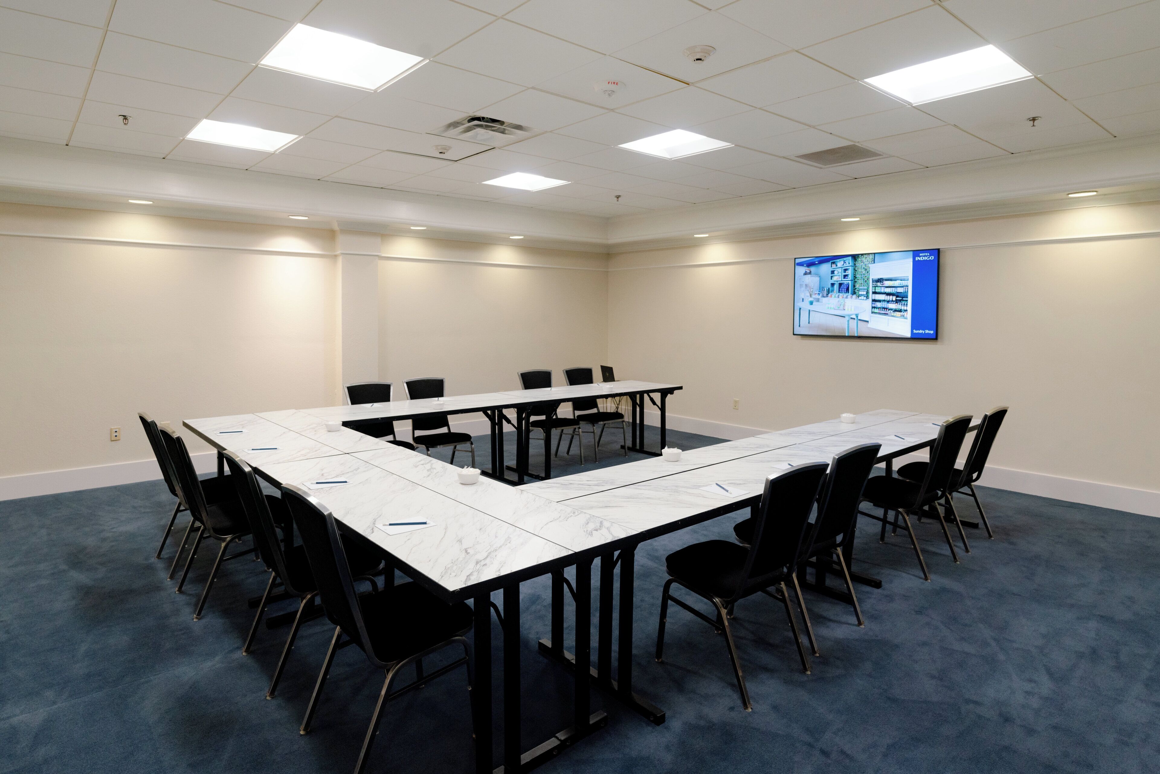 A conference room with a large table, black chairs, and a screen on the wall.