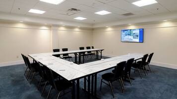 A conference room with a large table, black chairs, and a screen on the wall.