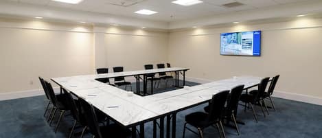 Une salle de conférence avec une grande table, des chaises noires et un écran mural.