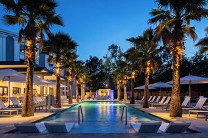 Un área de piscina con sillones de descanso y palmeras, rodeada por un edificio con un letrero que dice 'hotel indigo'.