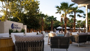 A hotel outdoor seating area with wicker chairs, a pool, and palm trees.