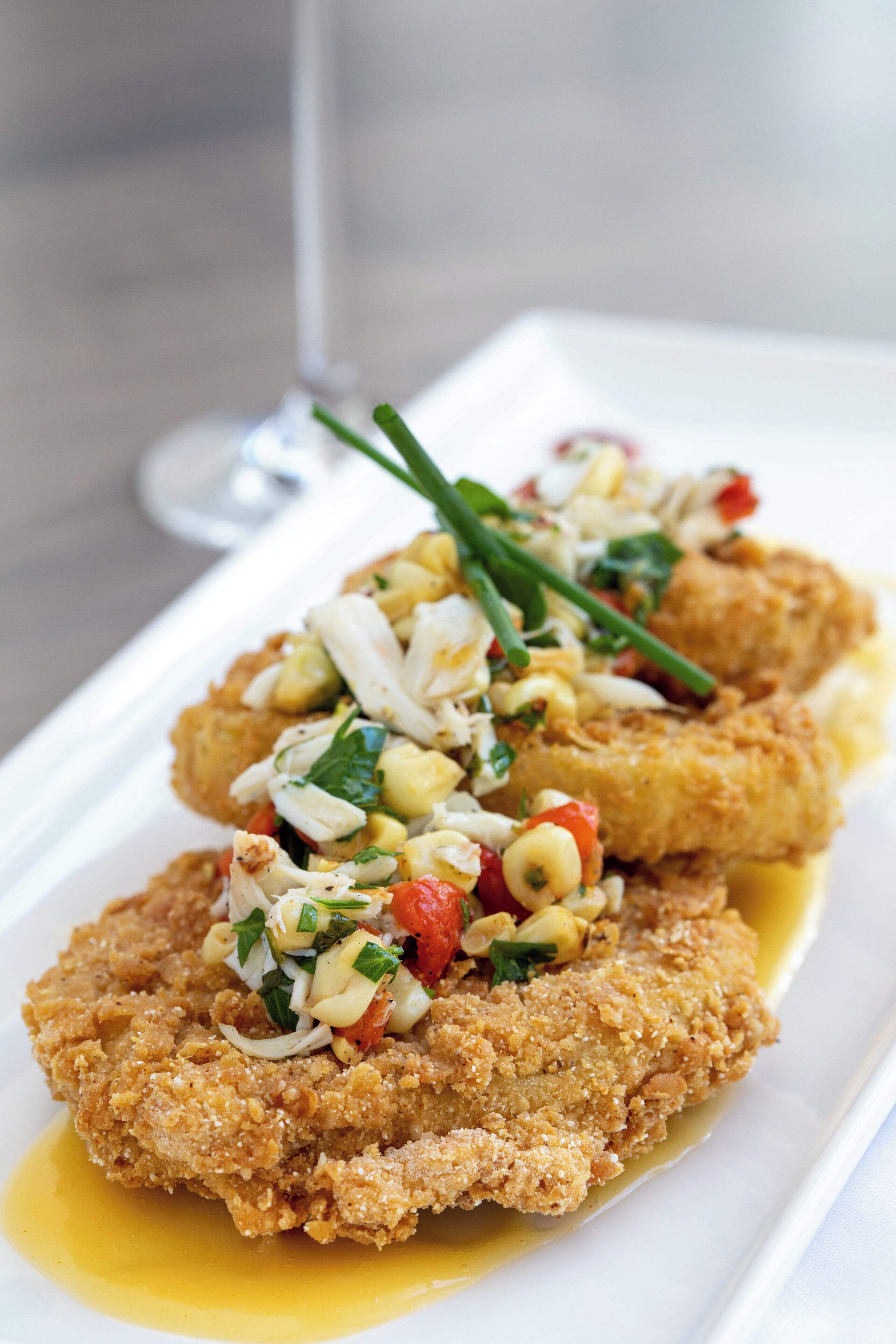 Prato com escalopes empanhados, molho e guarnição de legumes picados.