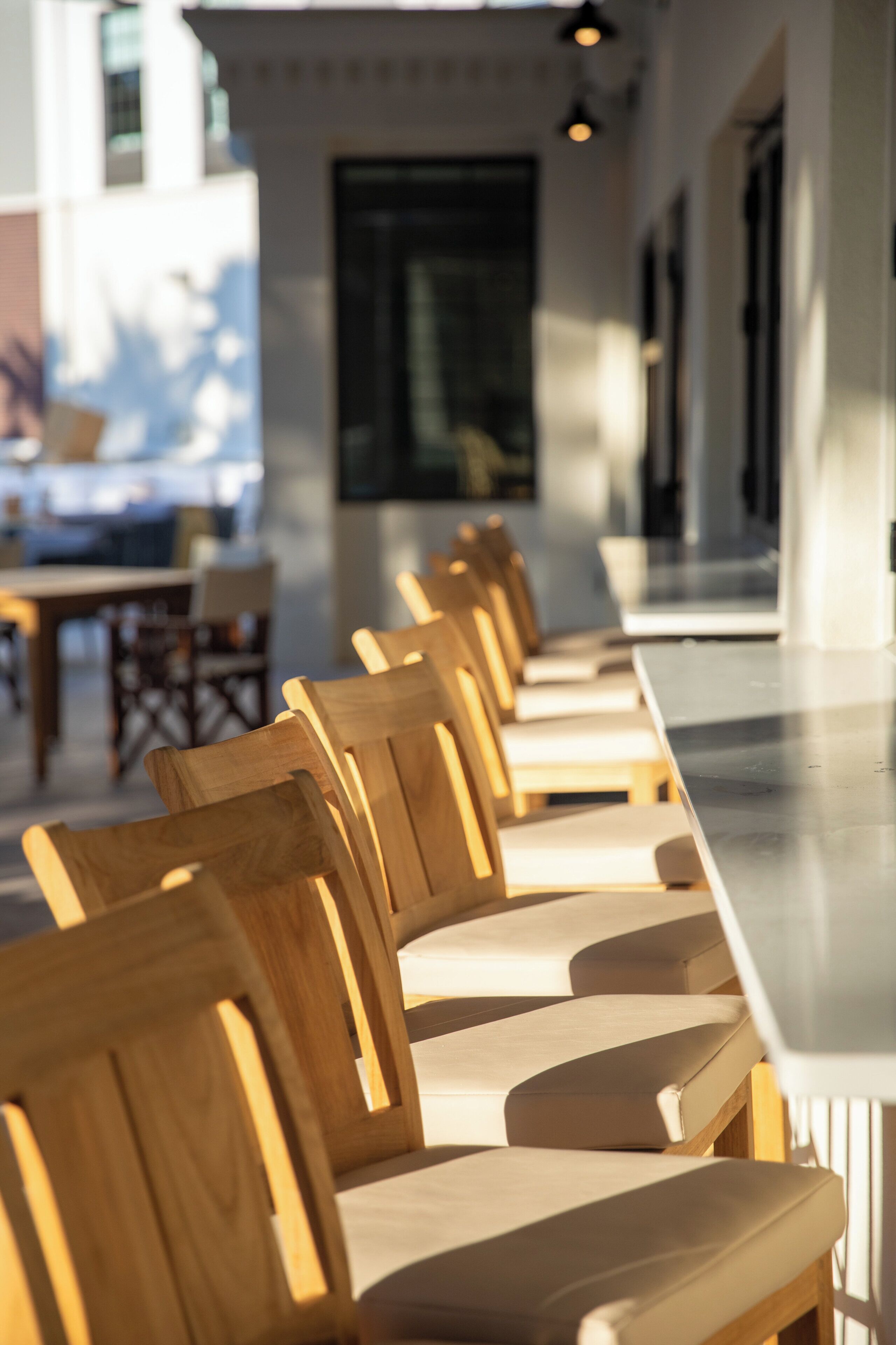 A row of wooden chairs with cushioned seats and backs, arranged in a line along a long counter.