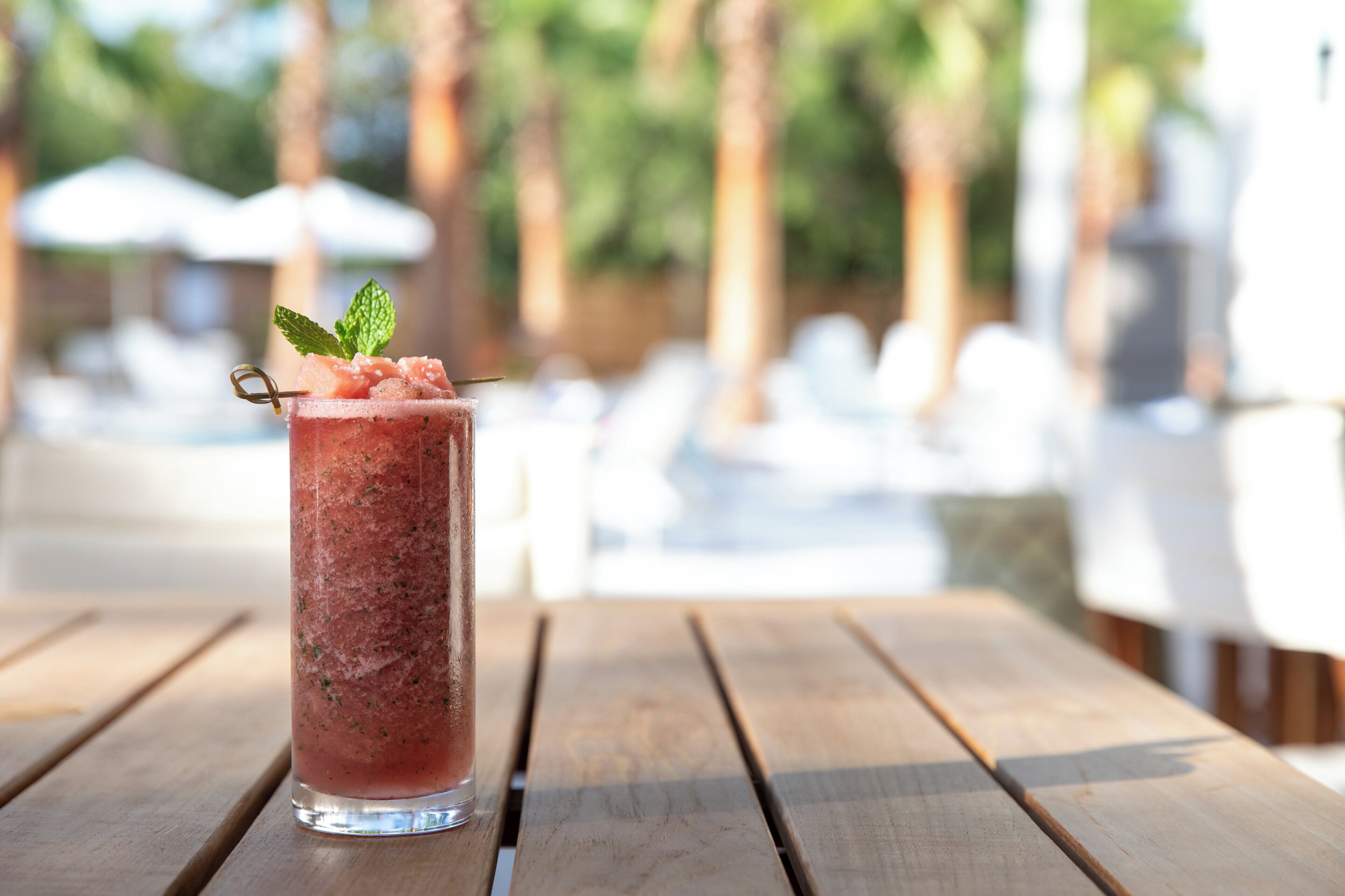 A tall glass of pink beverage with mint garnish on a wooden table.