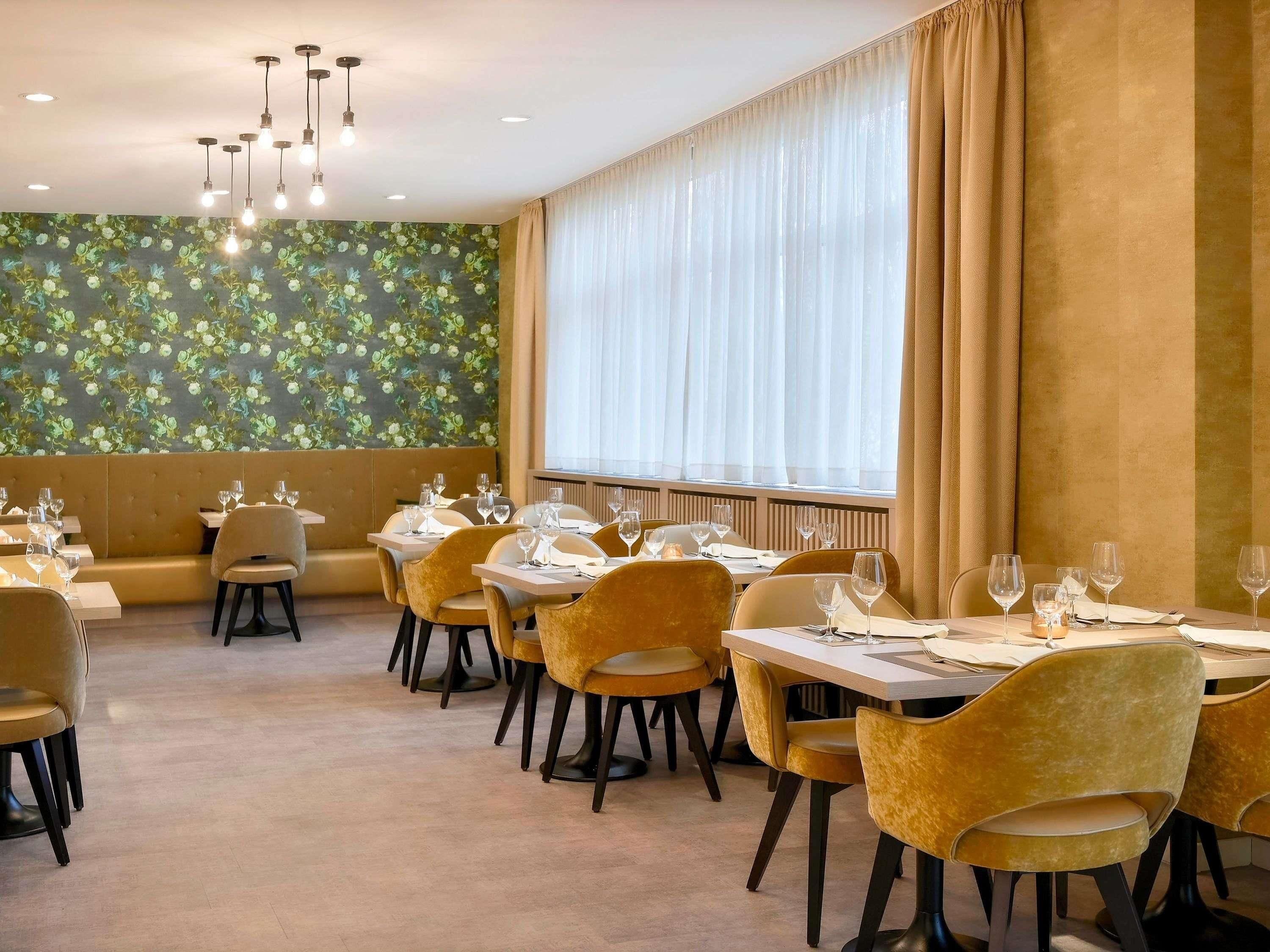 A restaurant with a long table, chairs, and a wall with a floral pattern.