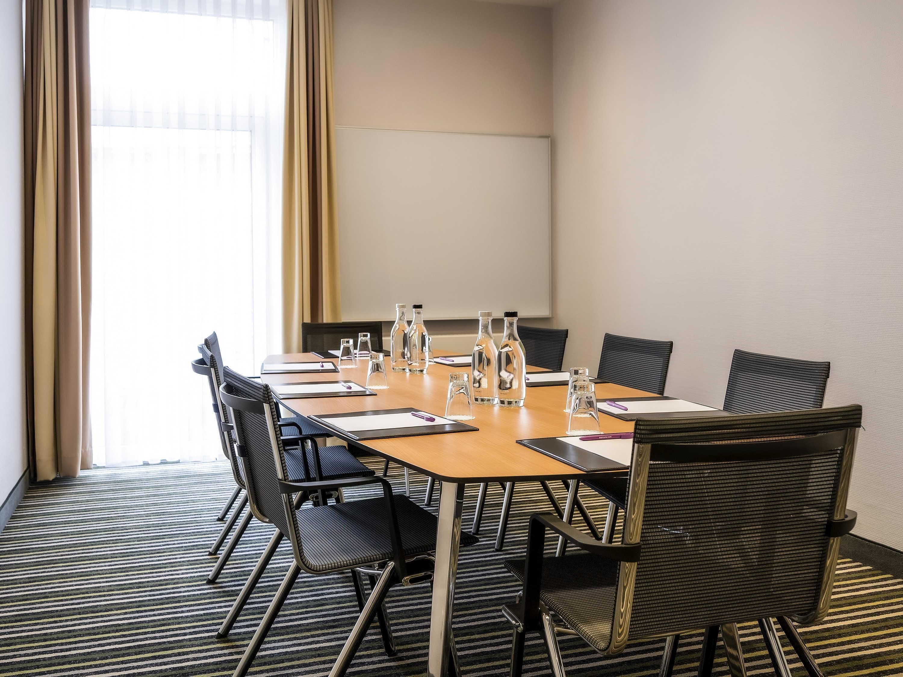 A conference room with a long table, chairs, water bottles, and a projector screen.