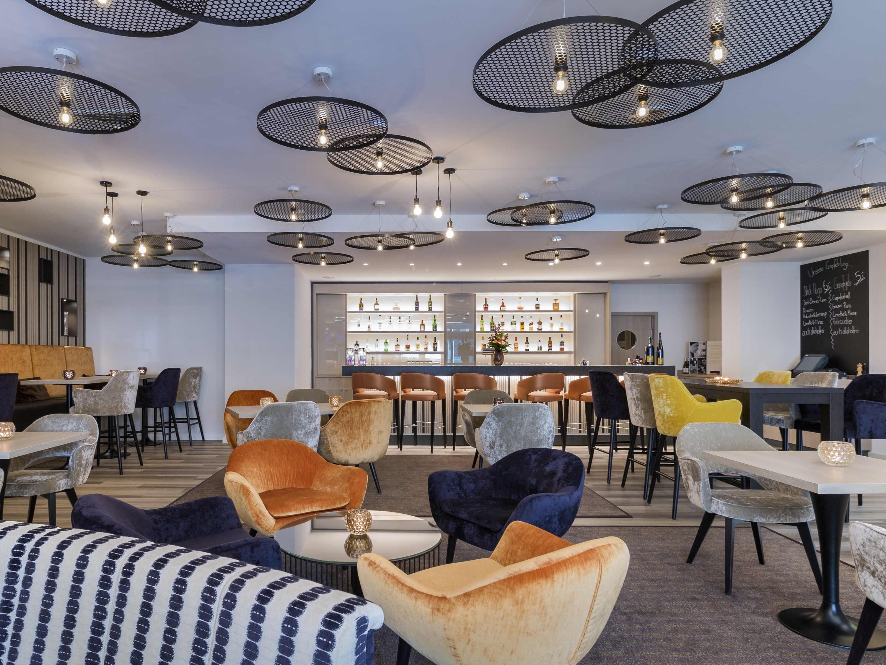 Een moderne barruimte met diverse zitmogelijkheden, waaronder banken en stoelen, en een bargedeelte met een selectie flessen.