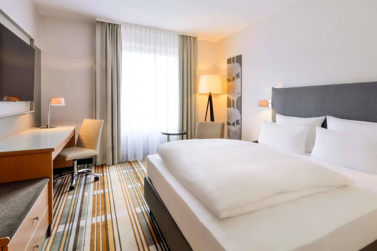 Habitación de hotel con cama, escritorio, silla, televisor y lámpara.