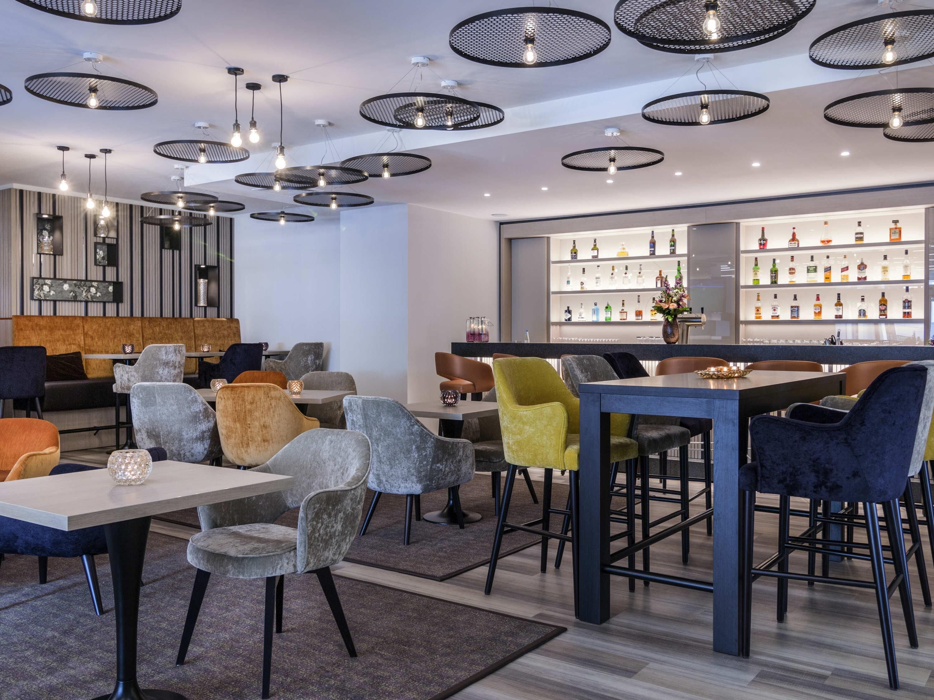 A modern bar area with round ceiling lights, a bar counter, and a variety of seating options including bar stools and cushioned chairs.