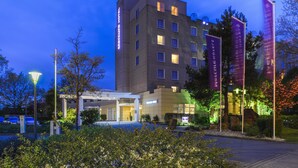 A hotel with a modern design, featuring a well-lit entrance and a parking area.