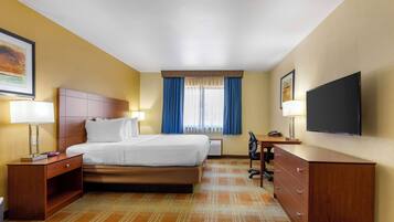 Habitación de hotel con cama, escritorio, silla, televisor y ventana con cortinas.