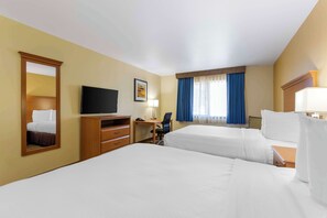 A hotel room with two beds, a desk, a chair, a television, and a window with curtains.
