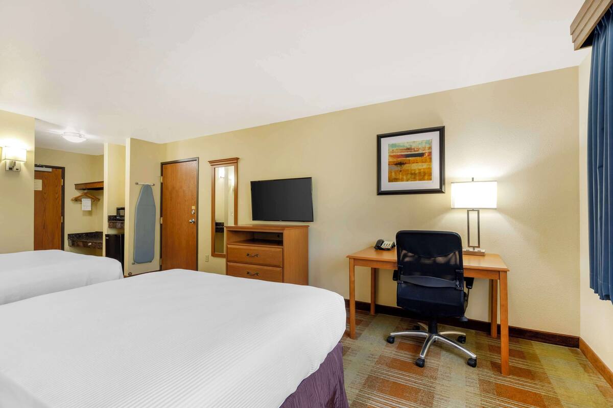 A hotel room with two beds, a desk with a chair, a television, a mirror, and a framed picture on the wall.