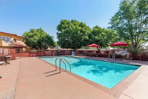 A swimming pool with a red fence, lounge chairs, and umbrellas.
