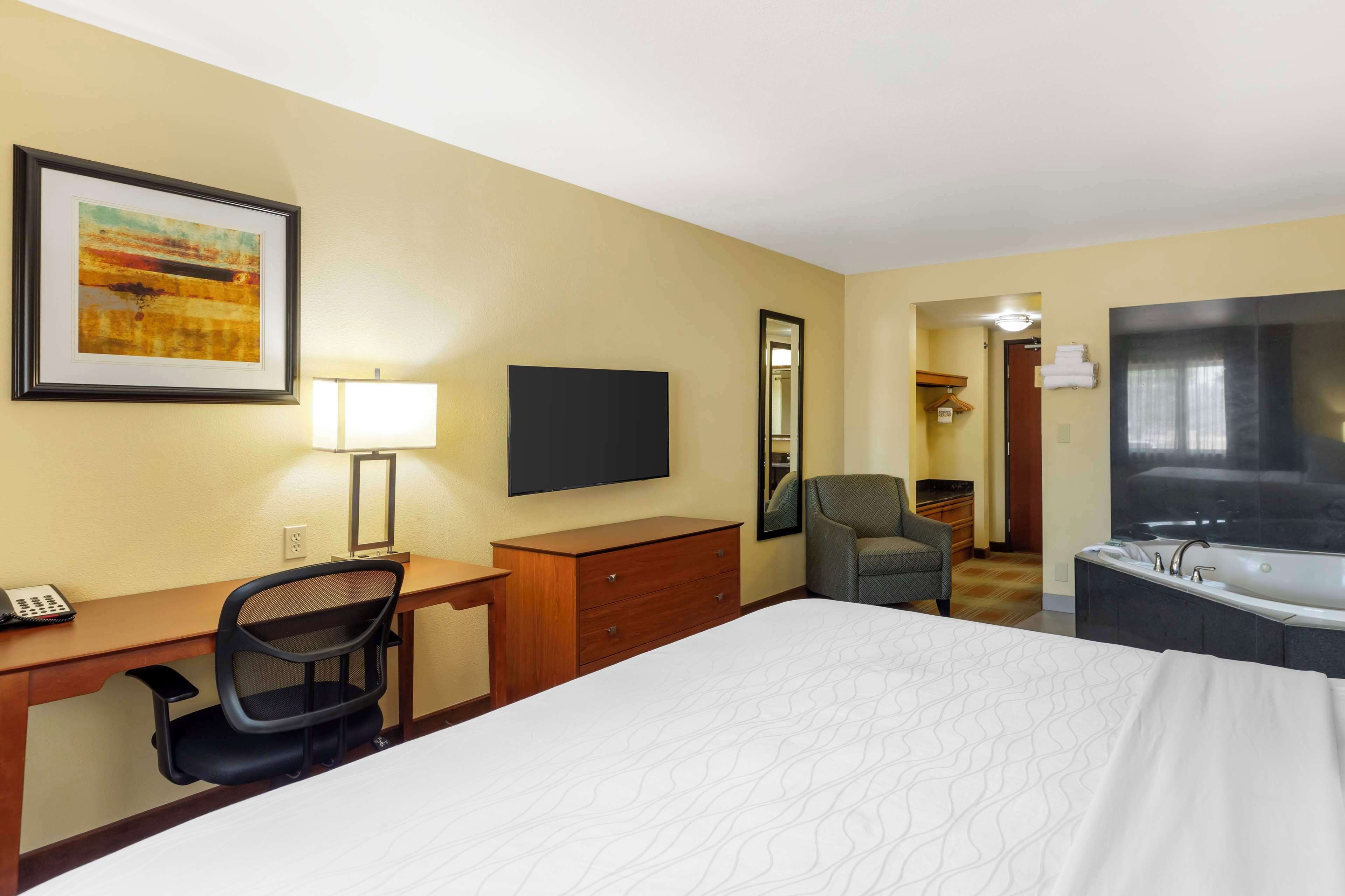 Habitación de hotel con cama, escritorio, silla, televisión, espejo y baño con bañera.