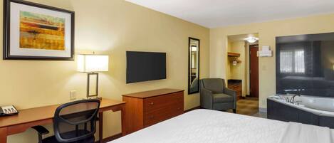 Habitación de hotel con cama, escritorio, silla, televisión, espejo y baño con bañera.