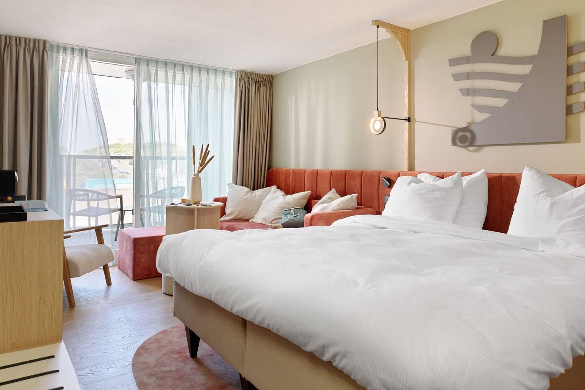 A hotel room with a large bed, a desk, a chair, and a view of the outdoors.