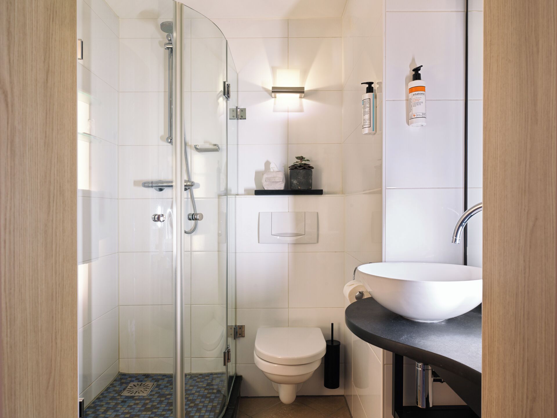 Un baño moderno con ducha envuelta en vidrio, inodoro blanco y lavamanos sobre encimera negra.