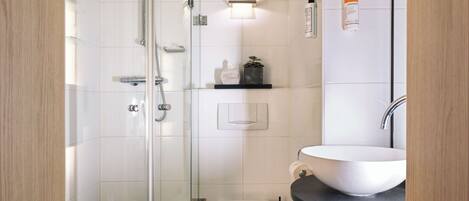Un baño moderno con ducha envuelta en vidrio, inodoro blanco y lavamanos sobre encimera negra.