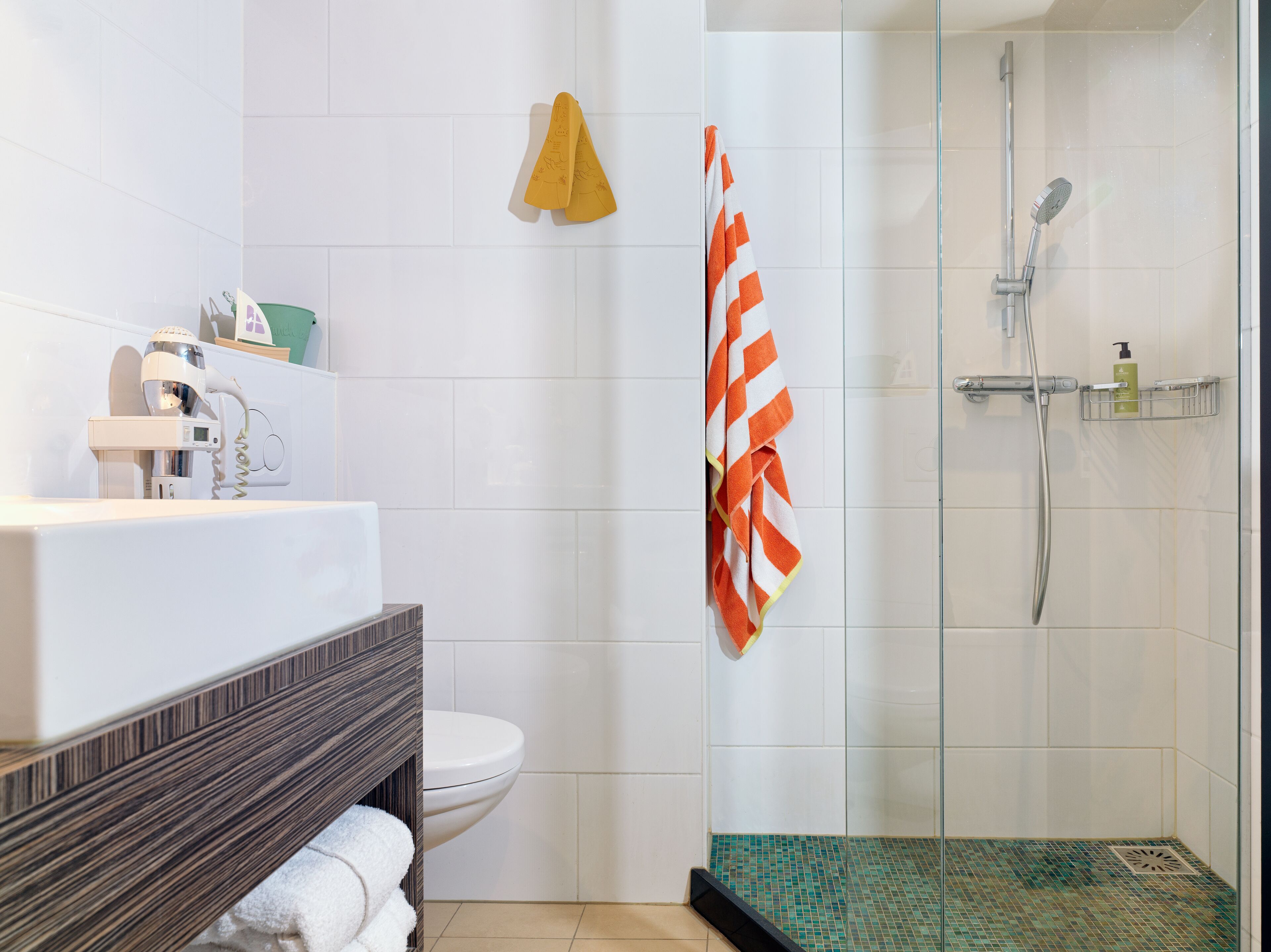 A modern bathroom with a glass shower enclosure, a white toilet, and a vanity with a towel rack.