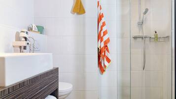A modern bathroom with a glass shower enclosure, a white toilet, and a vanity with a towel rack.