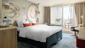 A modern hotel room with a large bed, a desk, and a balcony with a view. - Carlton Beach (The Hague)