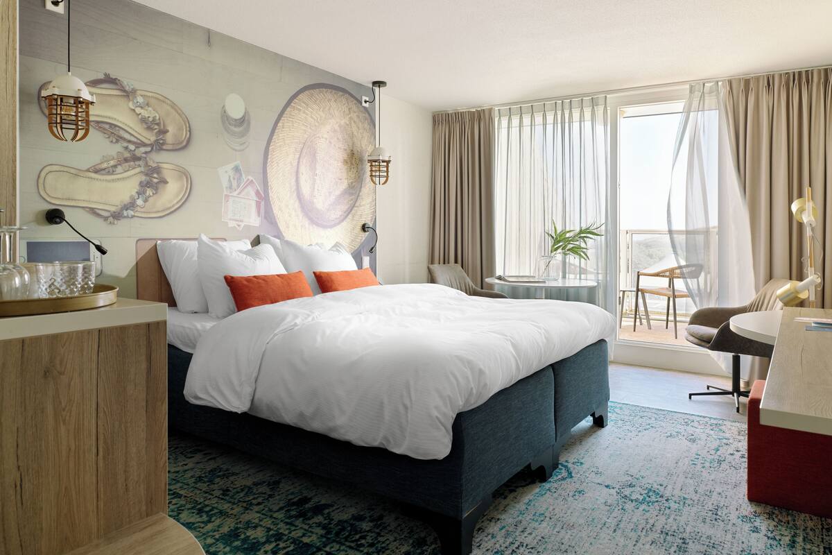 A modern hotel room with a large bed, a desk, and a balcony with a view.