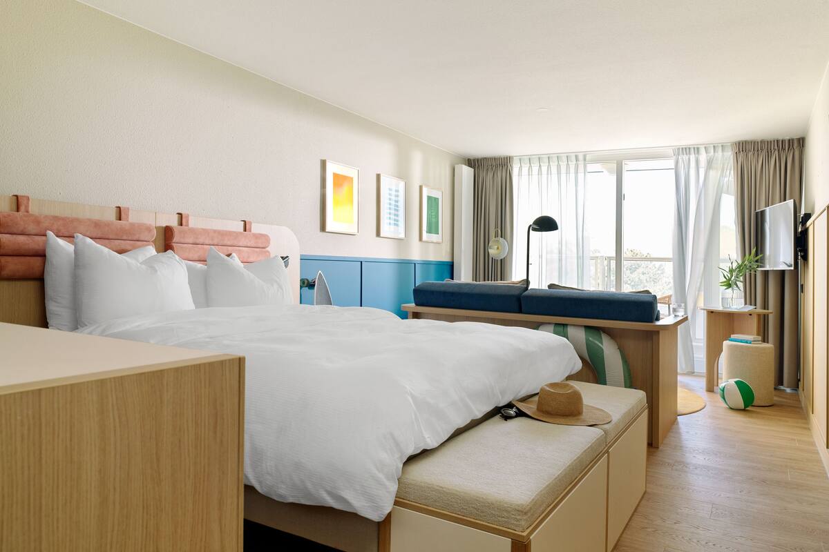 A hotel room with a large bed, a desk, a chair, a TV, and a window with curtains.