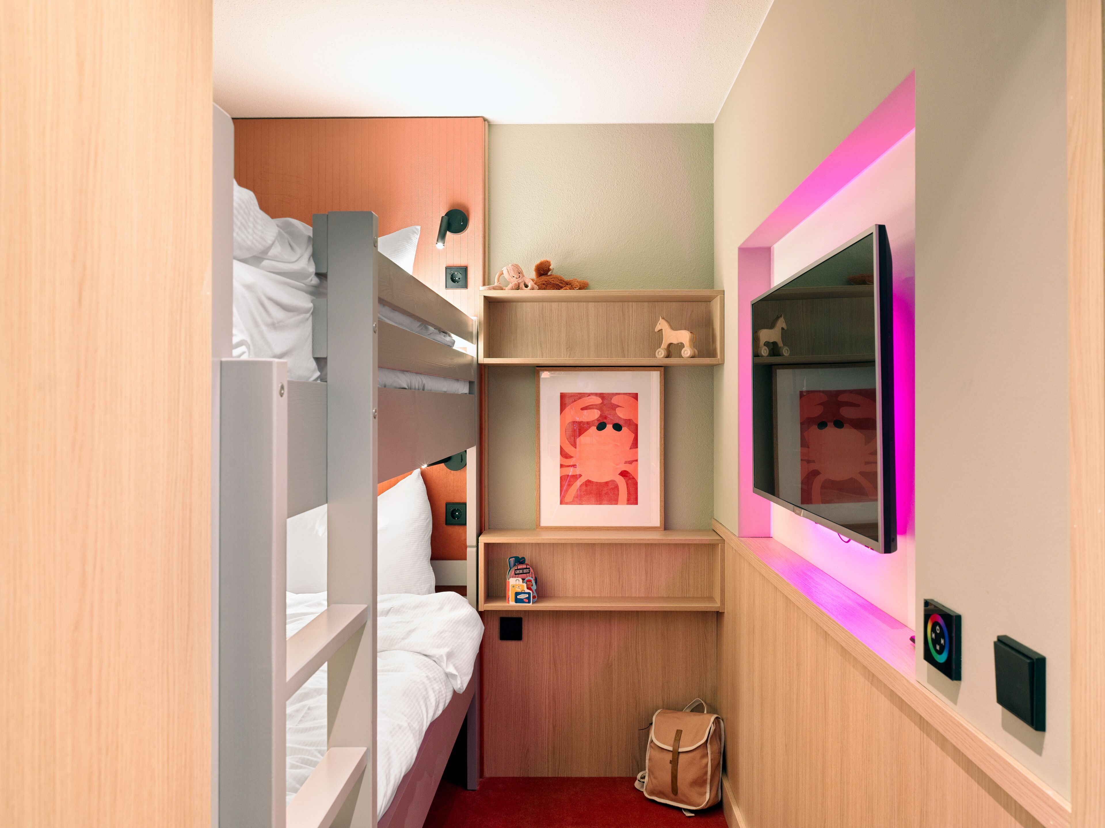 Ein kleines Zimmer mit Etagenbetten, einem Fernseher, einem Regal mit Spielzeug und einer kleinen Tasche.