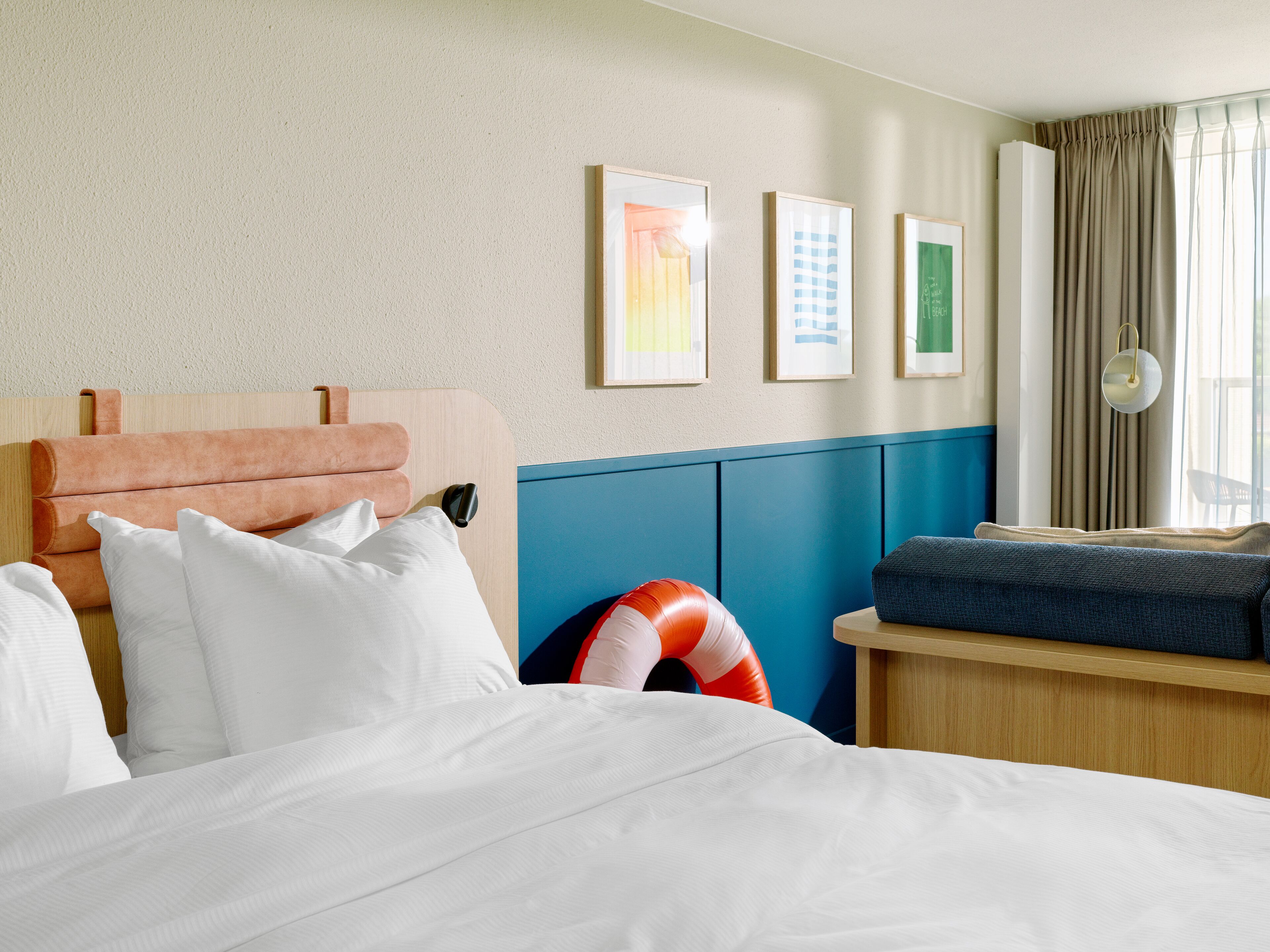 Een hotelkamer met een bed, nachtkastje, stoel en raam met gordijnen.