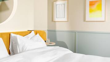 A hotel room with a bed, a bedside table, and two framed artworks on the wall.