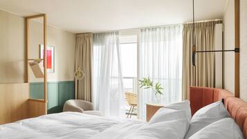 Une chambre d’hôtel avec un lit, une chaise, une petite table avec une plante et une fenêtre avec des rideaux.