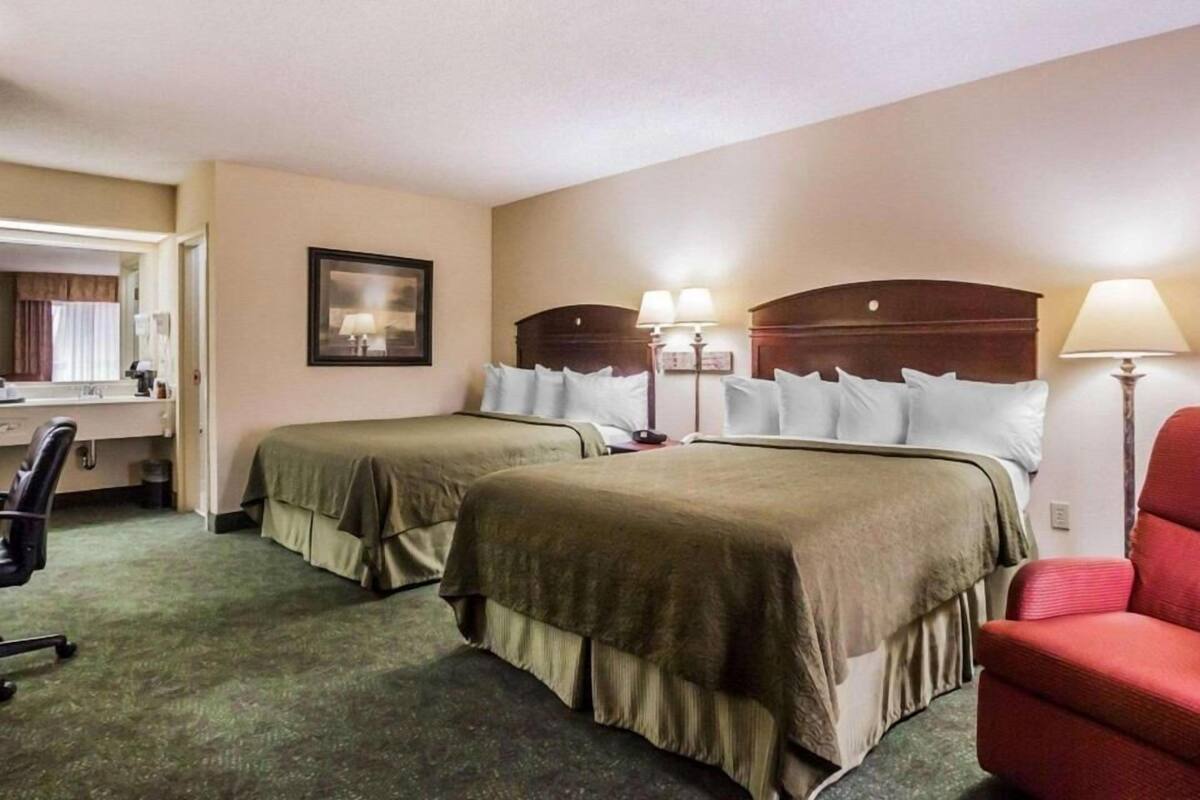 A hotel room with two beds, a desk, a chair, and a lamp.