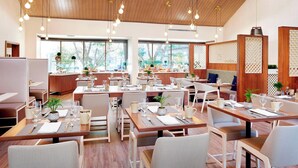 Un restaurante moderno con techo y paredes de madera, ventanas amplias y mesas y sillas ordenadas.