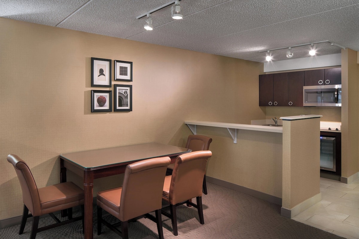 Una sala de conferencias con una mesa de vidrio y sillas de cuero, una kitchenette con armarios oscuros y cuadros en la pared.