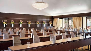 Une salle de conférence avec de longues tables, des chaises et un lustre.